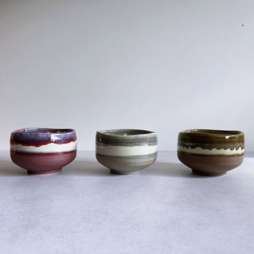 Three Japanese ceramic bowls with different coloured glaze on a white surface and background
