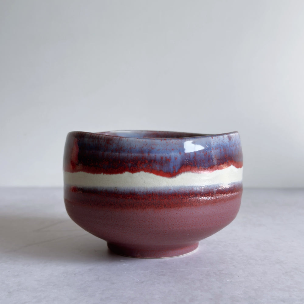 Japanese ceramic matcha bowl with dark purple and red glaze on a light grey background