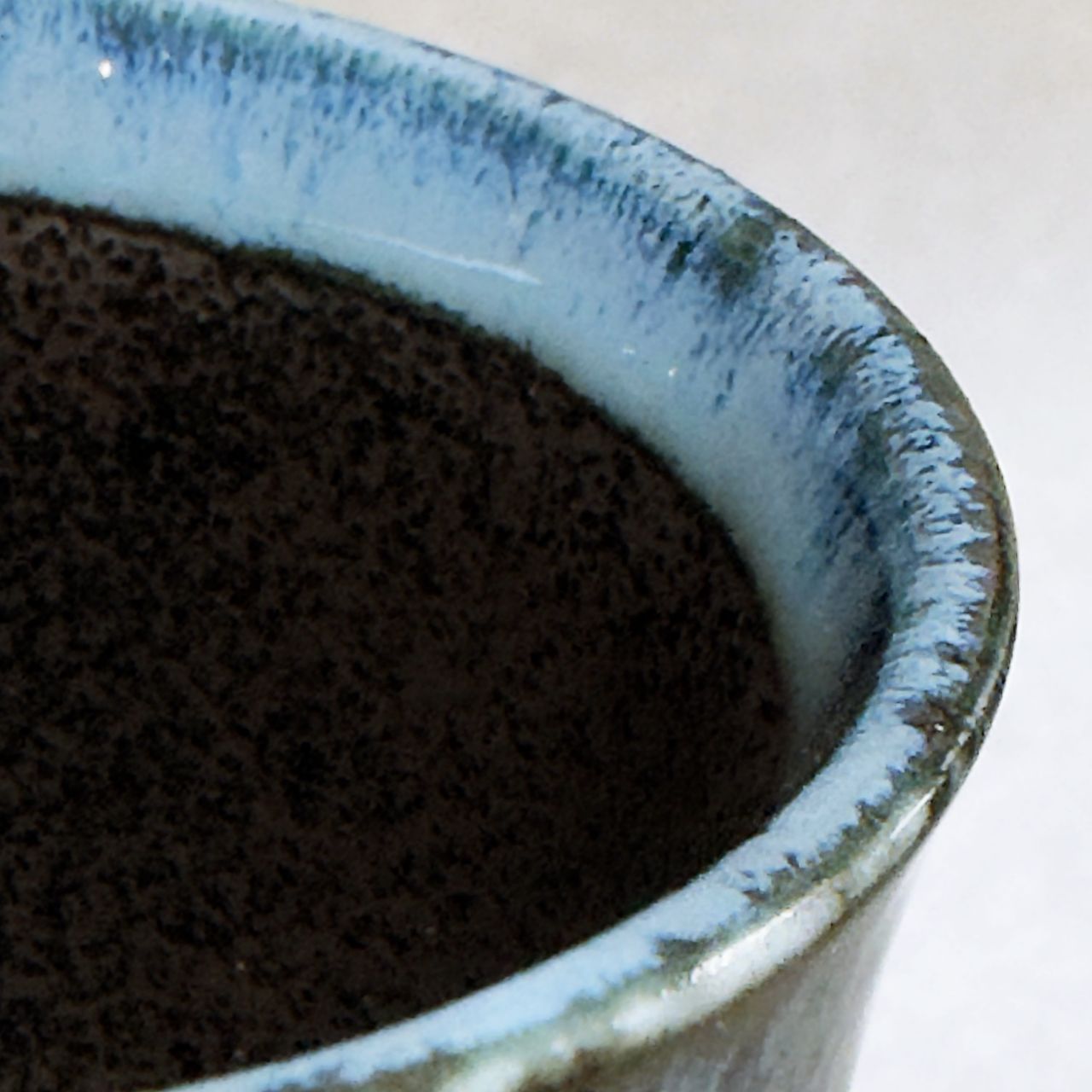 Close-up of a ceramic cup showing a dark brown speckled interior and a light blue glazed rim with a glossy finish.