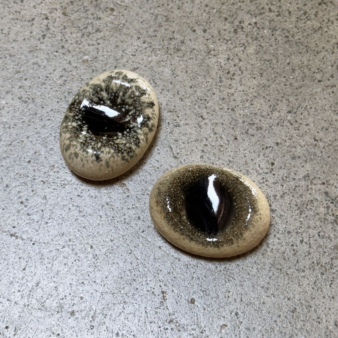 Two oval glossy chopstick rests with a mottled beige and black pattern, displayed on a textured grey surface.