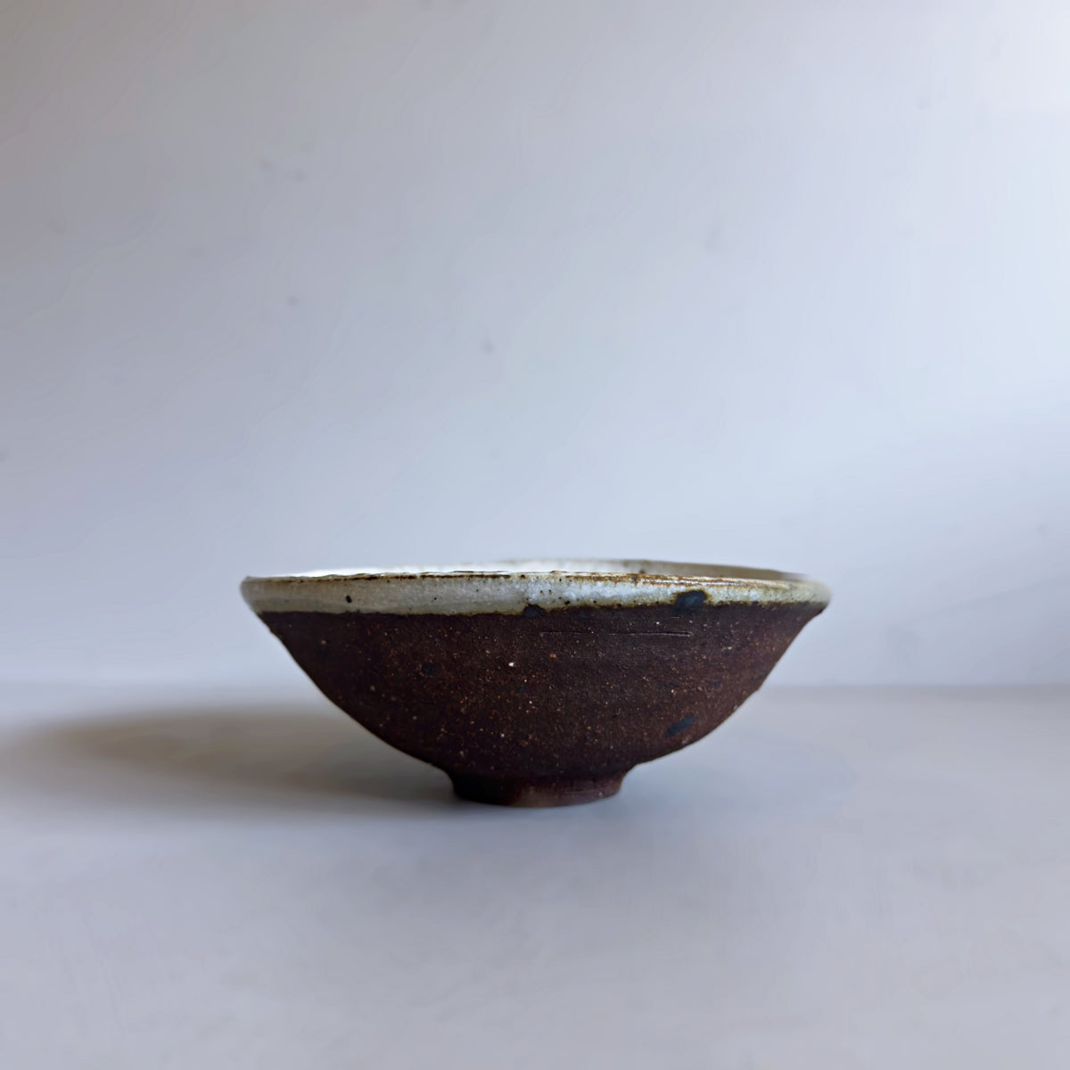 Side view of a vintage Japanese ceramic bowl with raw dark clay and a dipped white glazed rim, from Senju Living.