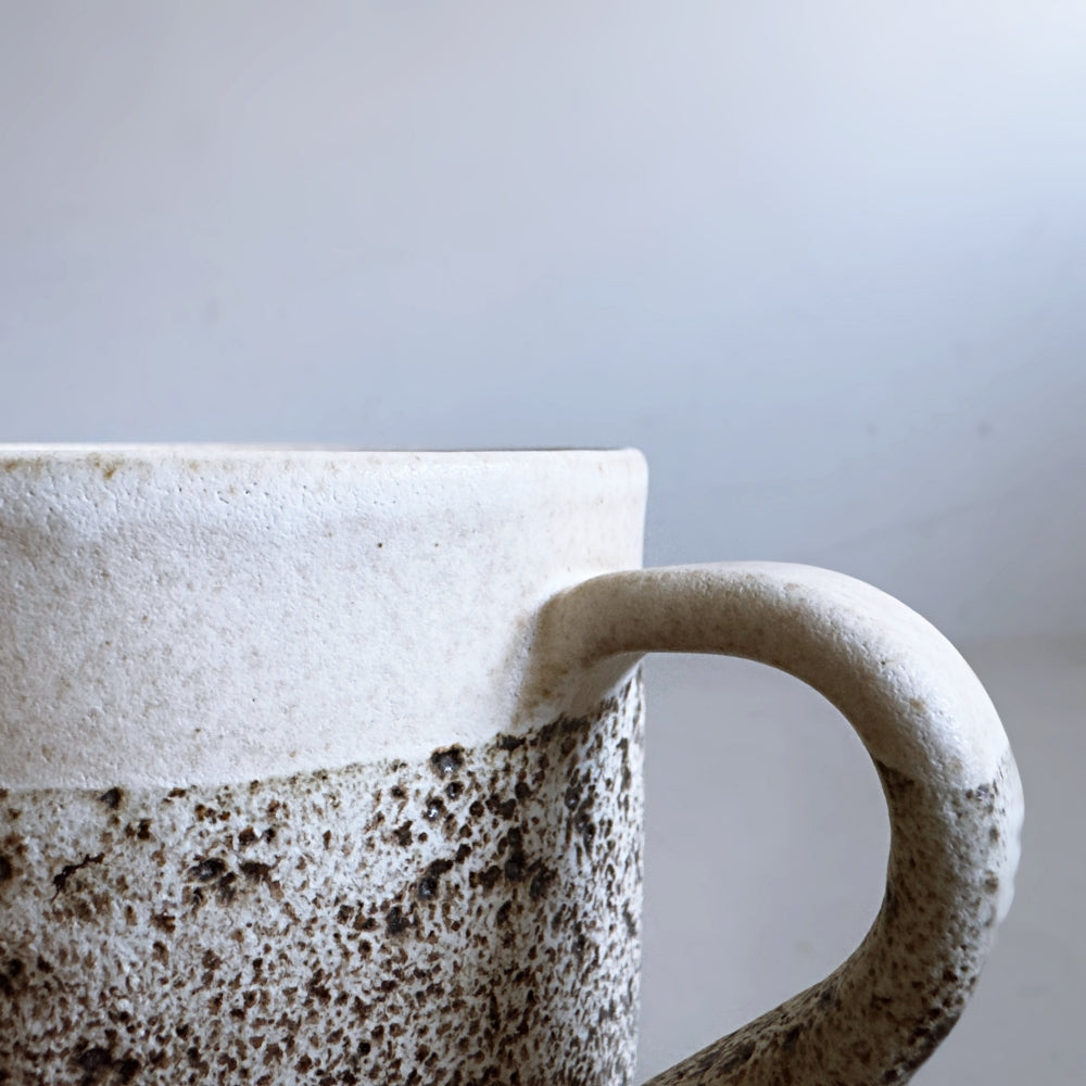 Close-up of a Japanese ceramic mug with a textured handle against a light grey background.