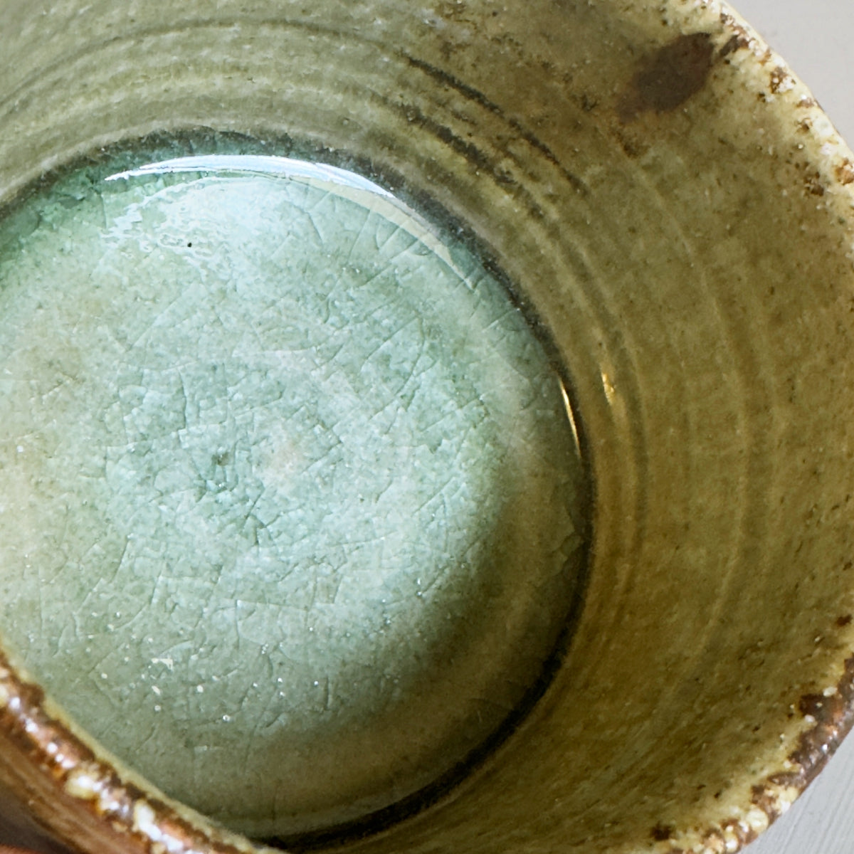 Close-up of a handmade ceramic Japanese matcha bowl with a textured interior glaze in pale mint green at the bottom and earthy brown tones.