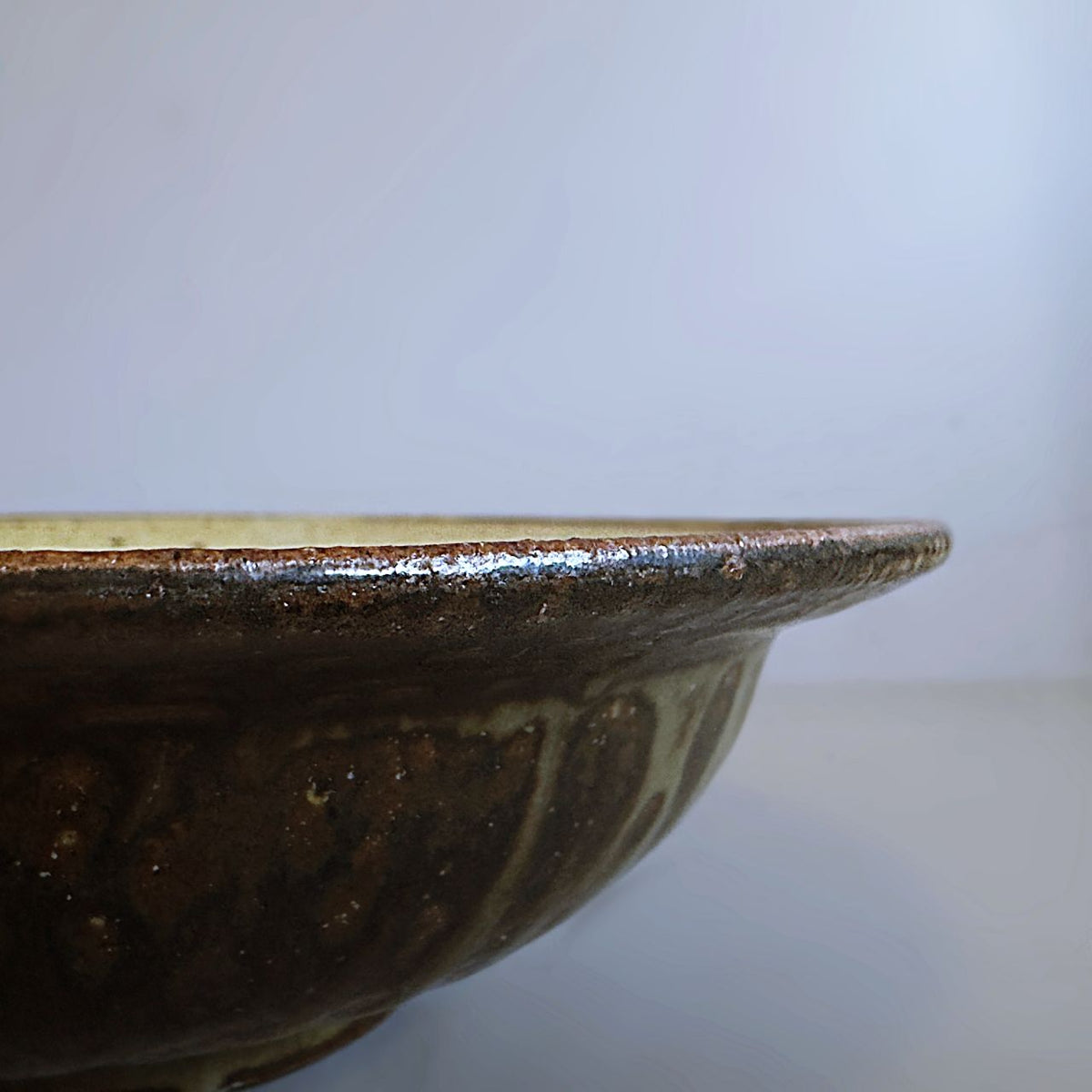 Close-up side view of the dark brown glazed rim and curved bowl profile from Senju Living.