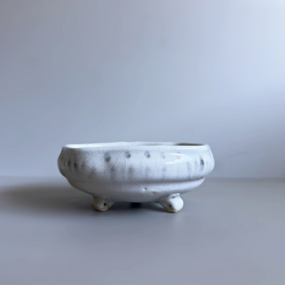 A front view of a square Japanese ceramic footed bowl with a speckled white and grey glaze, photographed on a neutral grey background.