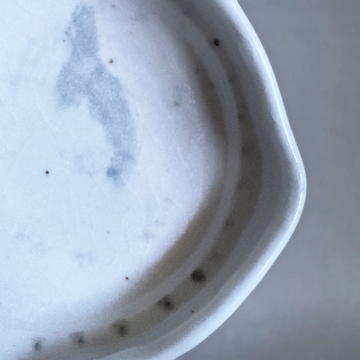 Close-up of a white Japanese ceramic bowl showing the glossy glazed interior with subtle grey speckling and a small row of dark spots along the rim.