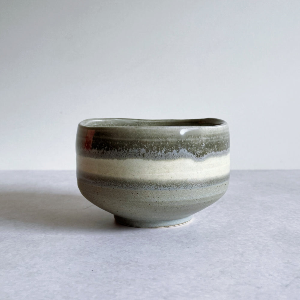 Ceramic matcha bowl with grey glaze on a light grey background.