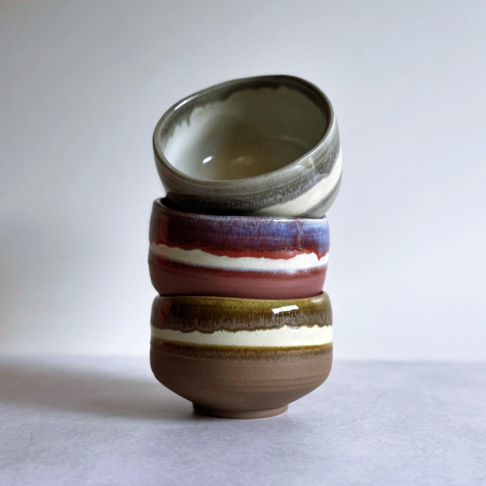 Stack of ceramic bowls with multicolored stripes on a white background