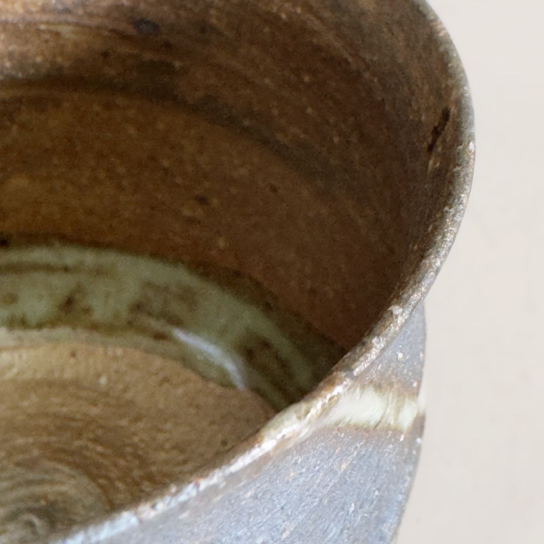 Close-up of the mug interior showing earthy brown clay and pale glaze pooling on a pale grey background.