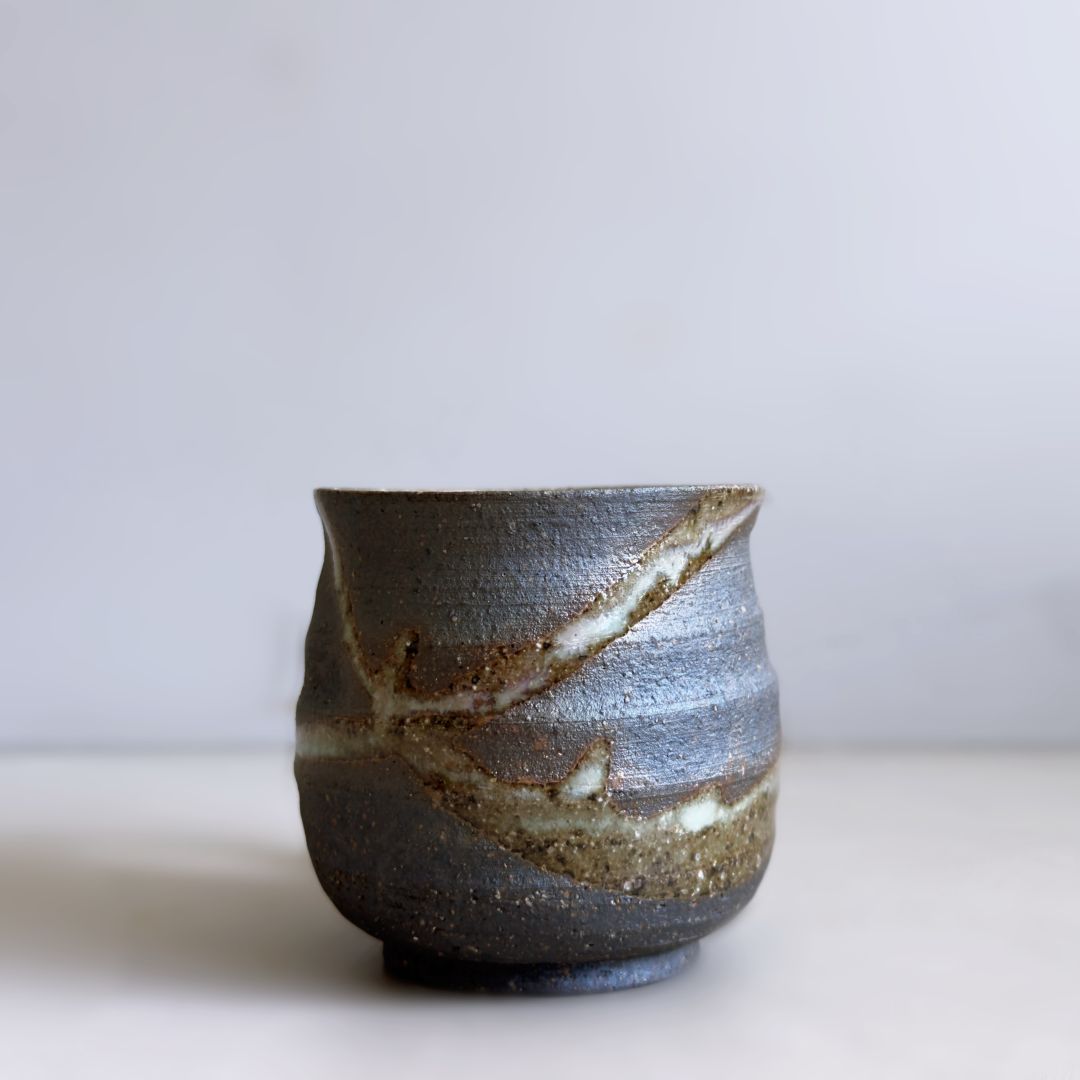 Side view of the handleless face showing dark clay and sweeping pale glaze bands on a pale grey background.