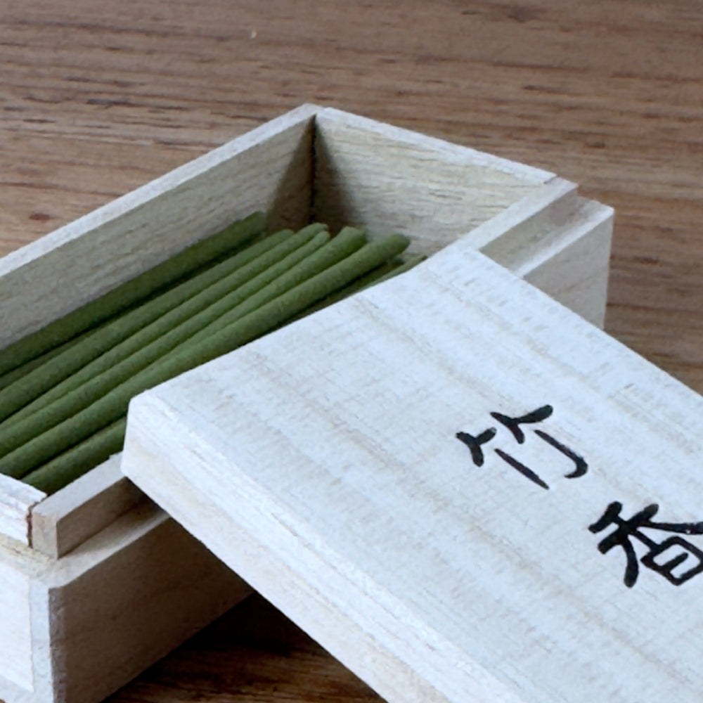 Close-up angled shot of green Takekou incense sticks inside an open timber box on a wooden surface, from Senju Living.