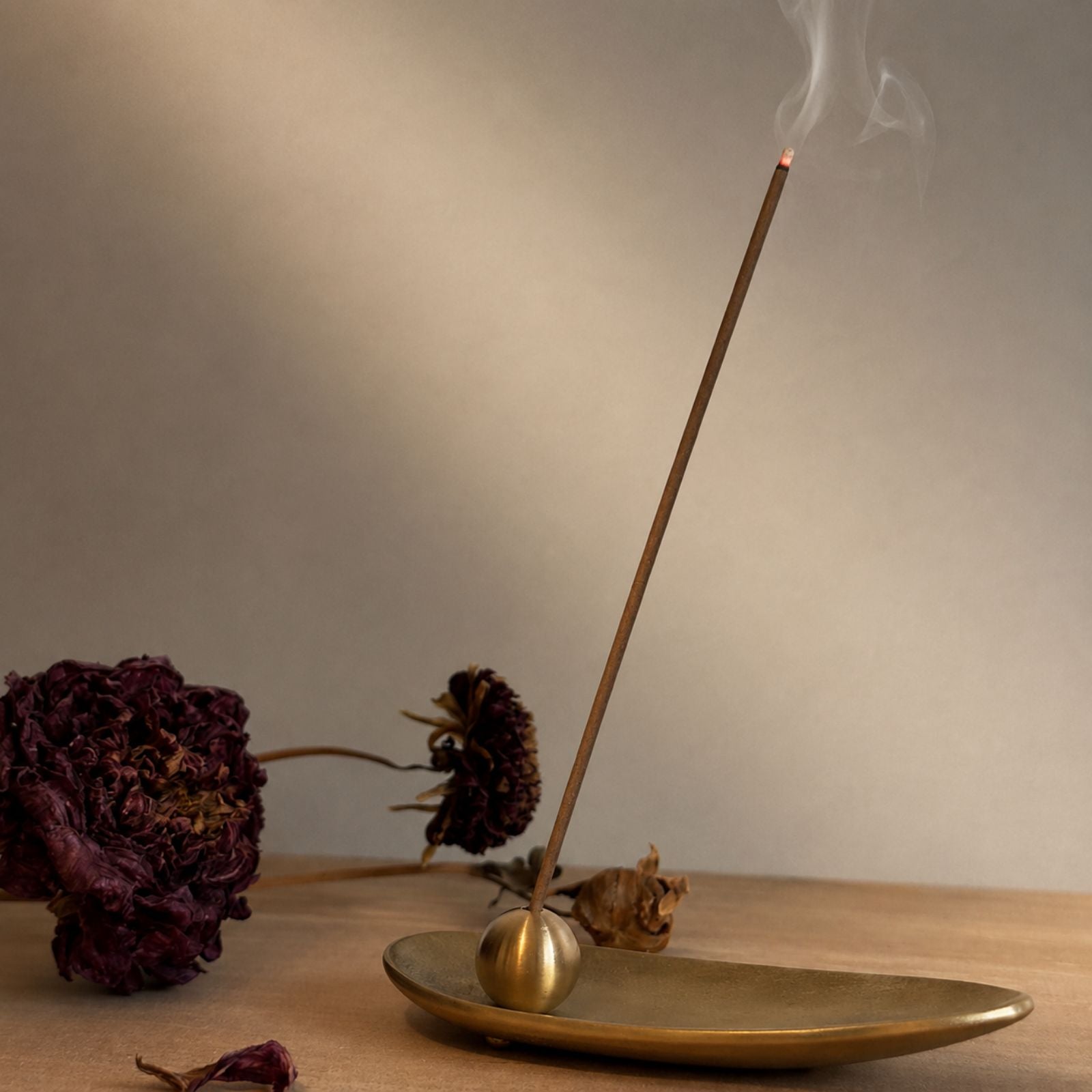 Lit Japanese incense stick gently smoking in a brass holder on a wooden table, minimalist Wabi-sabi home decor.