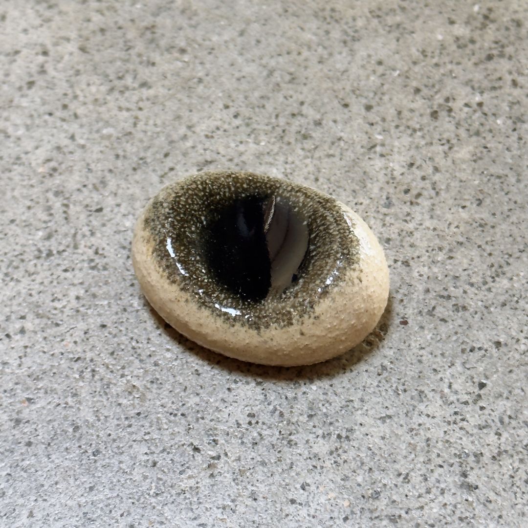 An oval Japanese ceramic chopstick rest with a dark  centre, resting on a textured grey stone surface.