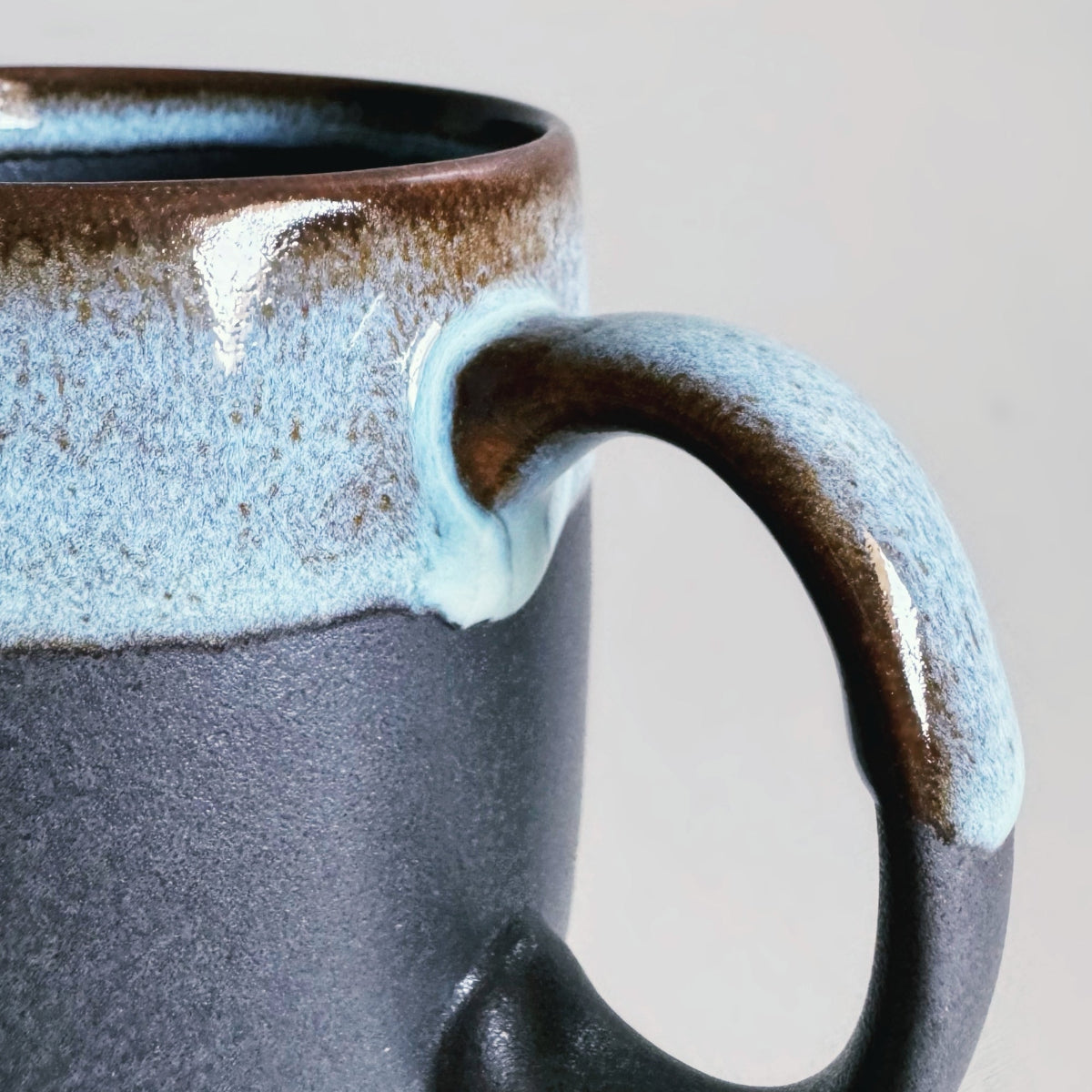 TOKA black ceramic mug detail featuring a pale blue dripping glaze on a large handle, handmade Mino ware.