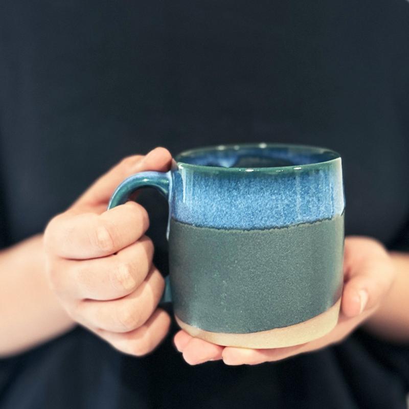 Hands holding a dark blue TOKA Japanese ceramic mug with blue and dark green glaze, handmade Mino ware from Gifu, Japan.