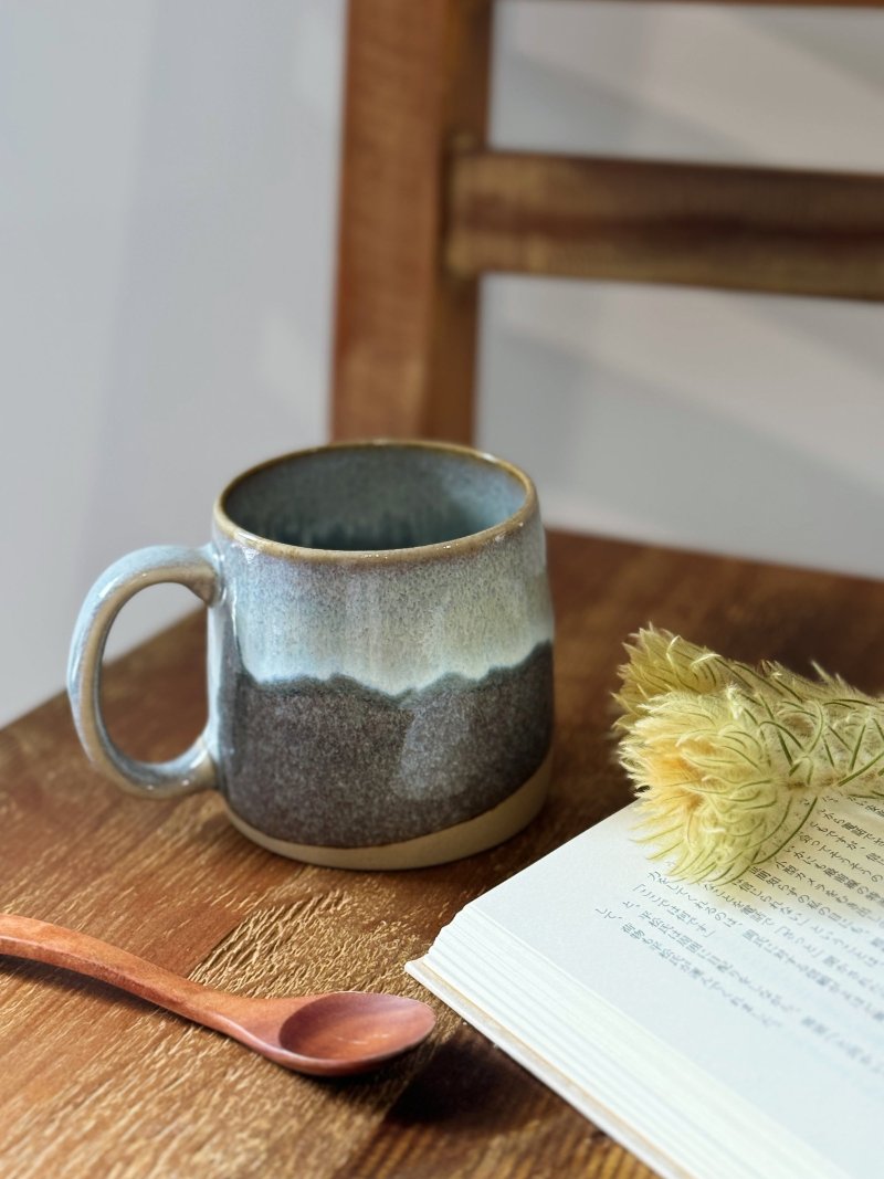 Grey TOKA ceramic mug and wooden spoon beside an open Japanese book, warm minimalist Japandi styling.