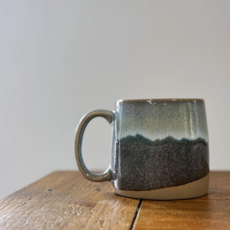 TOKA grey ceramic mug with dripping glaze on a rustic wooden table, minimalist Wabi-sabi lifestyle scene.