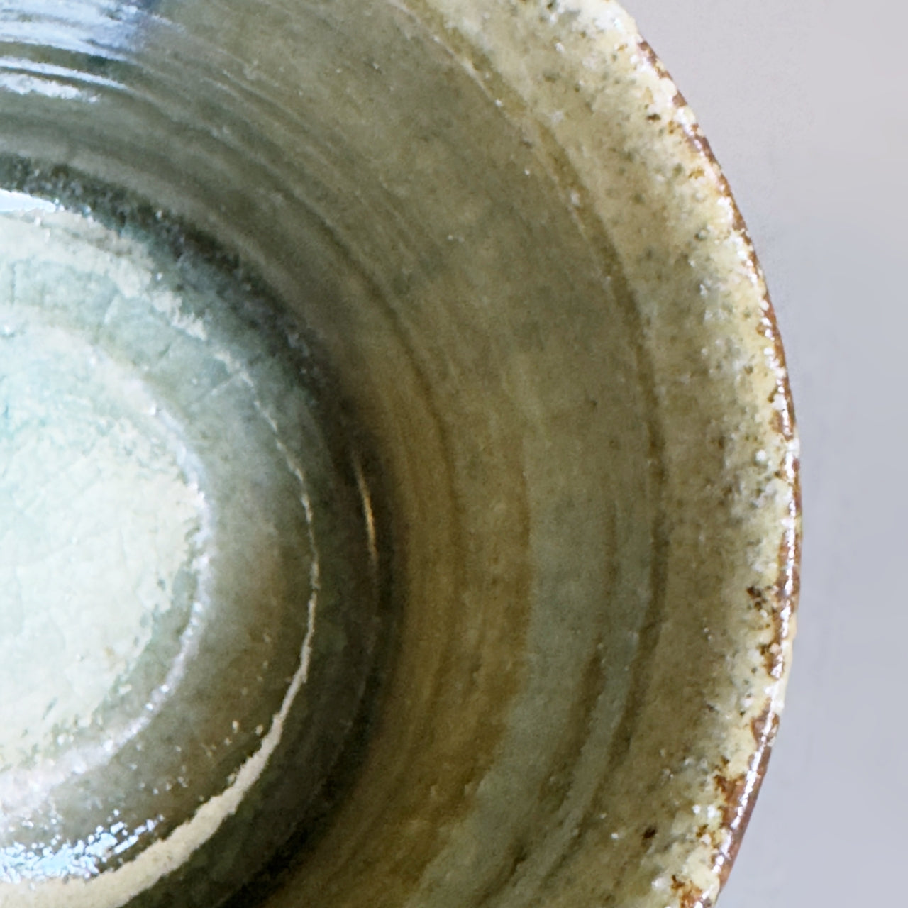 Close-up of the interior of a handmade Japanese ceramic cup with a textured, speckled glaze in earthy olive green, beige, and brown tones.